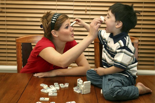 Child and teen playing with dominos at kitchen table.